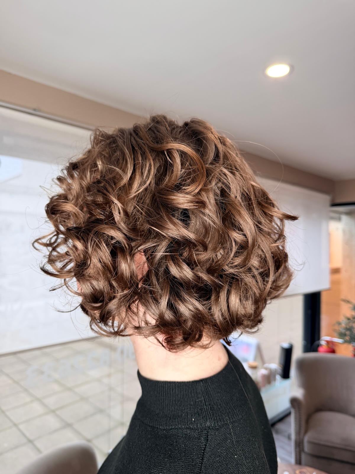 A short curly restyle with loads of bounce, seen from behind in the salon